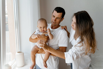 mom and dad are standing at the window with a baby, a young family