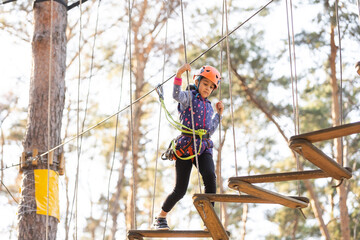 Naklejka na ściany i meble Happy school girl enjoying activity in a climbing adventure park on a autumn day