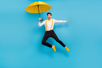 Full length portrait of energetic handsome guy hold umbrella flying isolated on blue color background © deagreez
