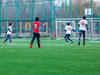 Boy in red white sportswear plays football on field, dribbles ball. Young soccer players teenagers with ball on green grass. 
