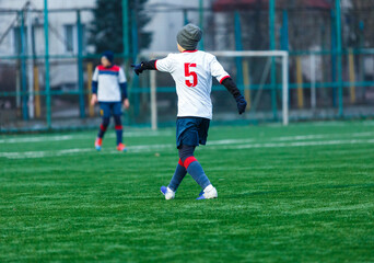 Young sport boys in white sportswear running and kicking a  ball on pitch. Soccer youth team plays football. Activities for kids, training	