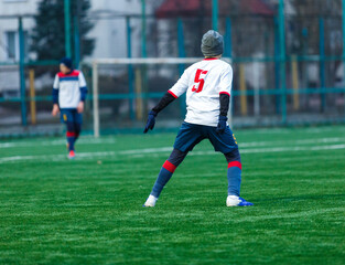 Obraz premium Young sport boys in white sportswear running and kicking a ball on pitch. Soccer youth team plays football. Activities for kids, training 