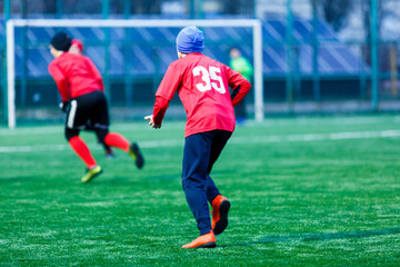 Obraz premium Boy in red white sportswear plays football on field, dribbles ball. Young soccer players teenagers with ball on green grass. 