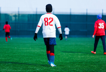Boy in red white sportswear plays football on field, dribbles ball. Young soccer players teenagers with ball on green grass. 
