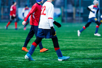 Boy in red white sportswear plays football on field, dribbles ball. Young soccer players teenagers with ball on green grass. 