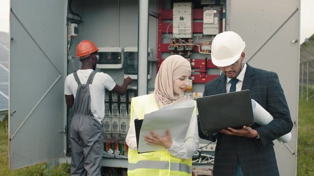 Electrical Systems Equipment Power Distribution Cabinet. Multiracial people examining process of green energy production. Power transformer. African american technician standing behind near switchgear