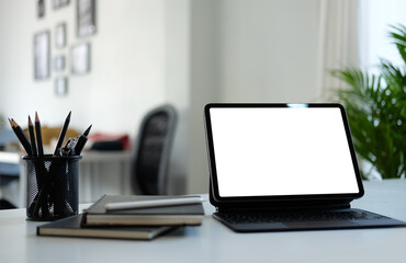 Modern workplace with computer tablet, notebook and pencil holder on white office desk. Blank screen for your advertising text.