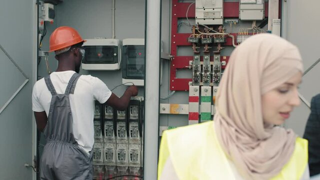 Power transformer. Electrical Systems Equipment Power Distribution Cabinet. Multiracial people examining process of green energy production. African american technician standing behind near switchgear