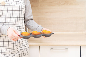 Caucasain woman holding tray with freshly made cupcakes or maffins at the kitchen