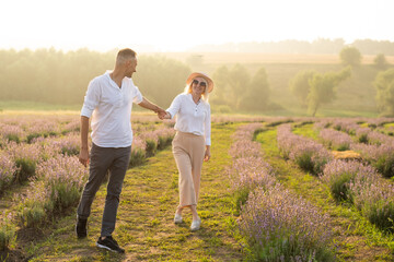 Smiling young couple embracing at the lavender field, holding hands, walking.