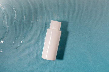  White cosmetic bottle in a blue pool with water and waves. Spa skin care.