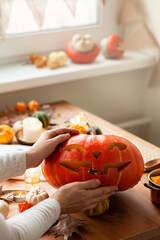 Woman carves a pumpkin for handmade Jack-O-lantern at home for Halloween party decoration. Concept of holiday seasonal handmade decor. Autumn colors, faceless, close-up