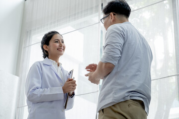 Doctor smile and the patient discuss together in front of glass window with curtain in the room at day time.