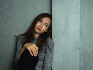 Young woman sitting sad against wall, depression emotion, looking space in dark room, Portrait of young beautiful woman or female or girl sitting expression depression emotional alone