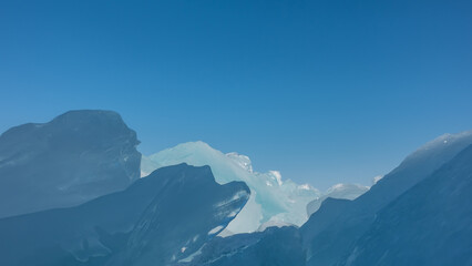 Fototapeta premium Ice hummocks against the sky. Close-up. The glare of the sun on the edges. Light and shadows. All shades of blue. Baikal. Copy space. Full screen