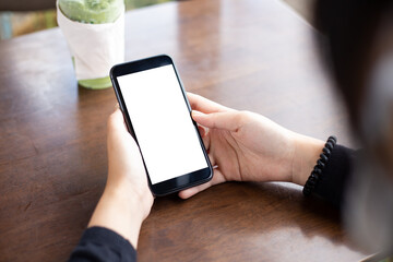 Woman hand using smartphone In the coffee shop Screen blank with clipping path ,Top view mockup image of girl holding mobile phone with empty white screen