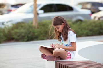 A teenage girl draws a sketch in the city. Educational plein air