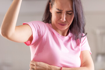 Woman can smell herself as she sweats with sweat patches in her armpits visible on a pink t-shirt