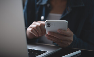 Closeup of business woman using mobile smart phone and working on laptop computer with digital tablet on office table at home.