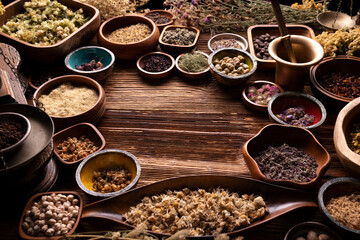Natural medicine background. Assorted dry herbs in bowls and brass mortar on rustic wooden table.