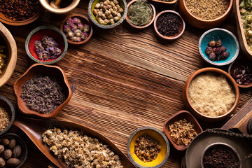 Natural medicine background. Assorted dry herbs in bowls and brass mortar on rustic wooden table.