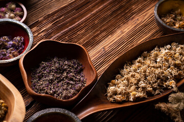 Natural medicine background. Assorted dry herbs in bowls and brass mortar on rustic wooden table.