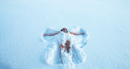 50-year-old woman lies enjoying in a swimsuit, in the snow in the form of an angel. The concept of...