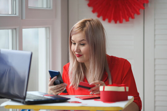 A young woman  orders gifts online via phone. February 14 celebration online. Shopping online on Valentine's Day