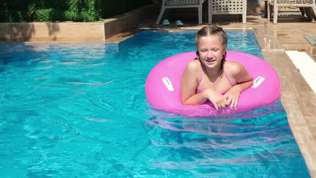 Little cute girl floating on pink inflatable ring in swimming pool. Summer travel hotel vacation