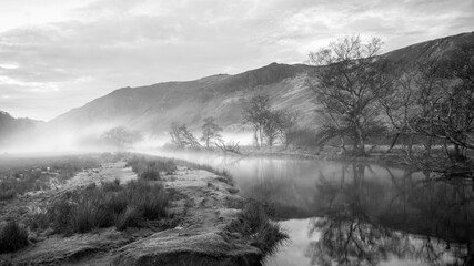 Black and white Stunning Autumn landscape sunrise image looking towards Borrowdale Valley from Manesty Park in Lake District with fog rolling across the landscape