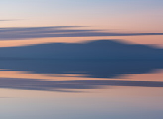 Intentional camera movement of sunset landscape image of distant mountains with pastel colors reflected in the calm ocean