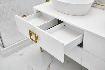 Elegant white cabinet with open drawer and shiny golden handles and leg with vessel sink in...
