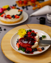 Pouring blueberry sauce onto delicious sweet cheesecake decorated with fresh berry fruits, and flowers on a wooden plate, for a birthday, Valentine day and celebration
