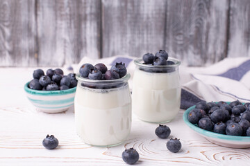 A healthy breakfast of Greek yogurt in glass jars and fresh blueberries at a rustic white table....