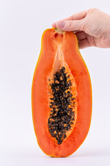 A hand holds a cut ripe papaya fruit with seeds on a light background, vertical photo, full depth of field