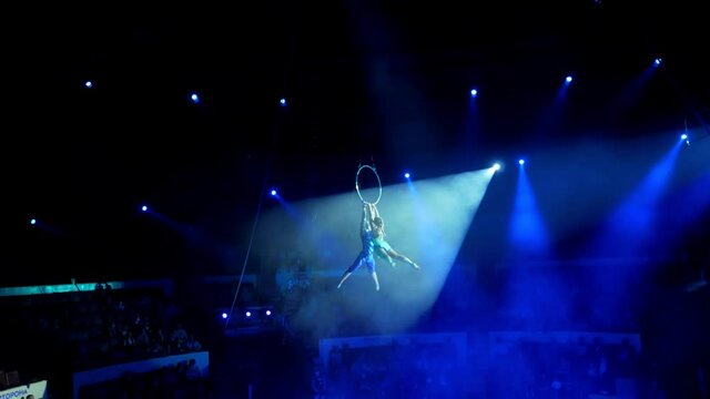 A duo of aerialists hang on an acrobatic ring, arranging a performance. Circus artists create shows for the audience. A frame with a contour light. Flexible, athletic, aerialists. Show