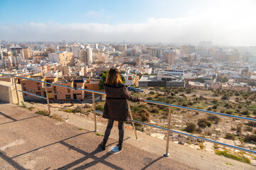 A young tourist girl looking at the city from the Cerro San Cristobal viewpoint in the city of Almeria, Andalucia. Spain. Costa del sol in the mediterranean sea