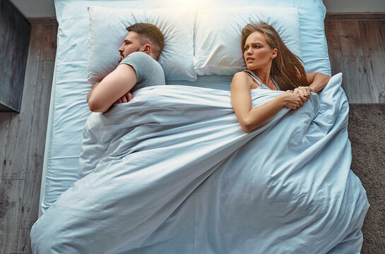 Young beautiful couple lying in bed, a girl with an emotion of anger pulls the blanket on himself, the guy ignores. Relationship problems. Top view.