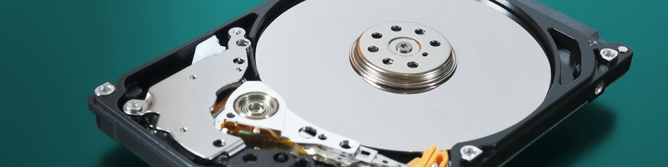 A disassembled open hard disk drive HDD of a computer or laptop lies on a turquoise matte surface. IT close up. Banner about computer hardware and equipment. Data storage headline. Macro