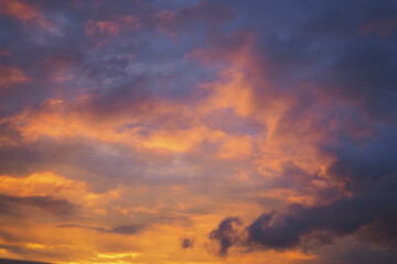 Cloudy sky at sunset. Dark violet and yellow natural background or wallpaper. The rays of the setting sun effectively illuminate the clouds. Beautiful and spectacular evening skies