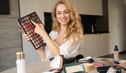 a woman blogs about make-up and beauty products. Gorgeous lady taking off makeup tutorial with makeup eyeshadow palette. Smiling girl teaches makeup using her phone. webcam view.