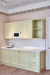 Small kitchen furniture set in classic decorative style with sink and microwave oven near white door in light spacious room