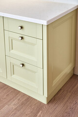 Classic chest of drawers with light green facades and acrylic solid surface countertop in light modern kitchen close view