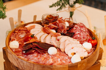 cold cuts on a round wooden plate with cheese and tomatoes. sausage, dried meat and jamon on a...