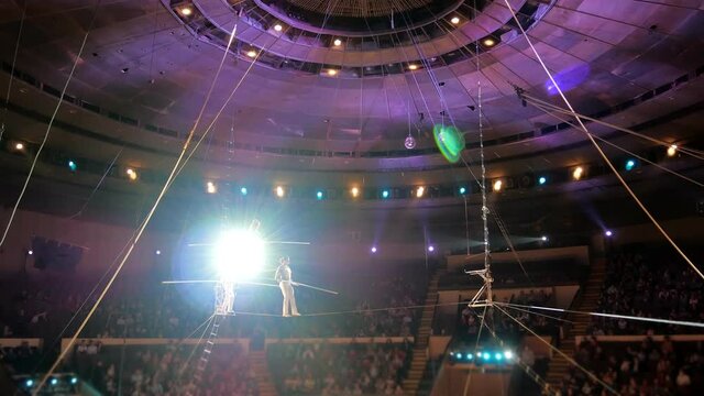 Performance of three aerial tightrope walkers gymnasts in white suits in the circus. Aerialists arrange a show for the audience under the dome of the circus, a tightrope walker walks on a rope.