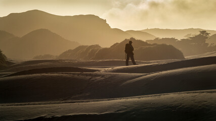 Fototapeta na wymiar Backlit of a backpacker standing on the sand dune on Wharariki Beach, South Island, New Zealand.