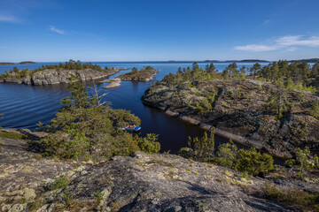 Landscape with a forest on stones over the lake. Sunny day at the lake. Reflection of the sky in the water. Pines on stones. The nature of the north.