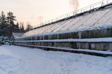Old orangery building in winter botanical garden or park. Greenhouse with glass walls covered with...