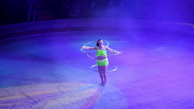 A circus artist performs in the circus arena with a lot of hula hoops, creates a show for the audience. Rhythmic gymnastics. A clever woman spins a lot of hula hoops on stage. Gymnastic circle