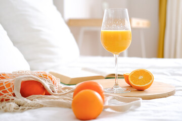 Oranges and orange juice in a glass on a white bed. Fresh oranges. Fruits lie on a white bed. Fruits close-up. Breakfast in bed. 